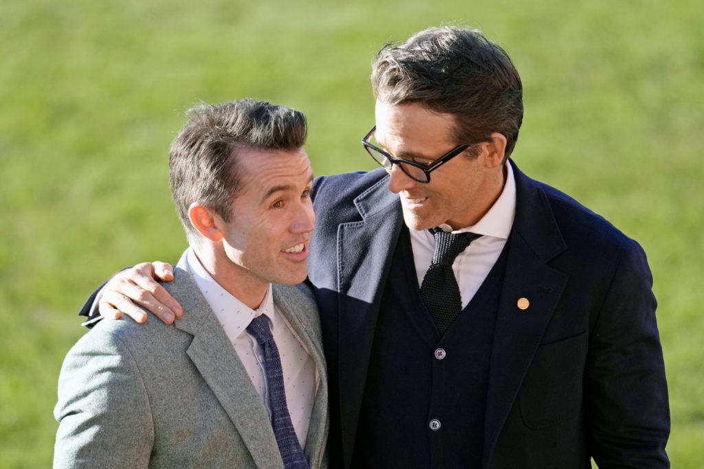 Rob McElhenney and Ryan Reynolds talk as they wait for the arrival of King Charles III and Camilla, Queen Consort, for their visit to Wrexham AFC