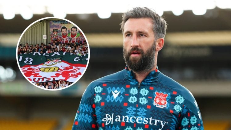 Ollie Palmer of Wrexham AFC warms up. Fans of Wrexham display a flag of their badge with a banner of owners Rob McElhenney and Ryan Reynolds.